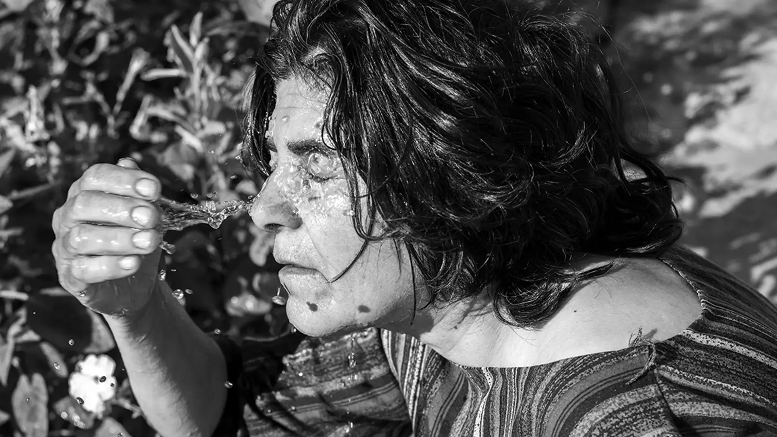 Black and white photo of a woman splashing water on her face.